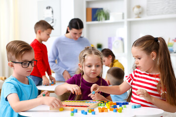 Fototapeta premium Cute children and teacher at white tables during lesson in elementary school