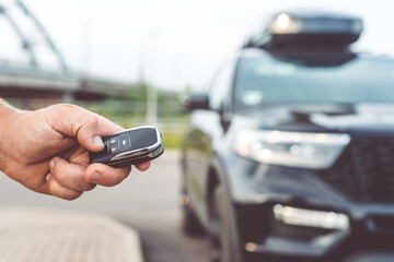 Close-up of a man unlocking a car using a key fob, with a black car parked in a car park in the background.