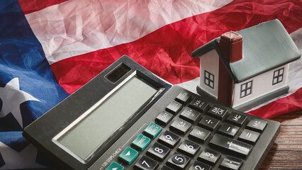 Miniature House Model and Calculator on American Flag, Symbolizing US Housing Market, Property Taxes, Mortgages, and Real Estate Finance in the United States.
