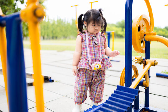 A cute little Asian girl is playing on exercise equipment in a park,Cute Asian children playing in playground for exercise in the morning smiling happily and outdoor exercise equipment in park.