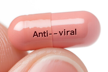 Obraz premium Close-up of an antiviral medication capsule, peach-colored, resting on a finger. The pill is labeled with 