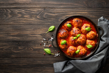Meatballs in tomato sauce with basil leaves on wooden table.