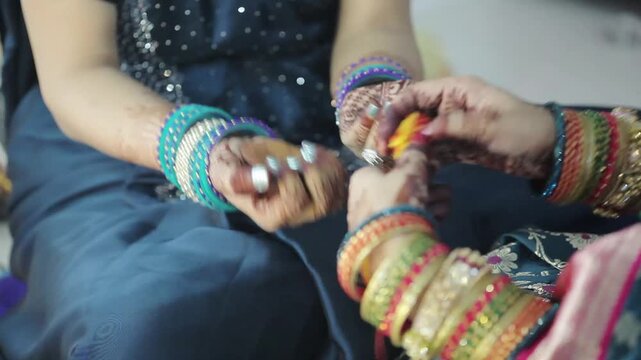 An Indian woman in a blue saree, tying sacred kalawa thread on another woman&rsquo;s wrist during a Hindu festival