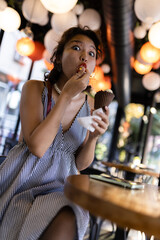 Young woman enjoying an ice cream cone in a modern cafe with hanging lanterns
