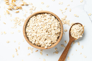 Rolled oats or oat flakes in a wooden bowl on white background.