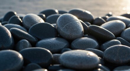 Close-up view of smooth, dark gray and black stones, possibly wet, glistening in the sunlight