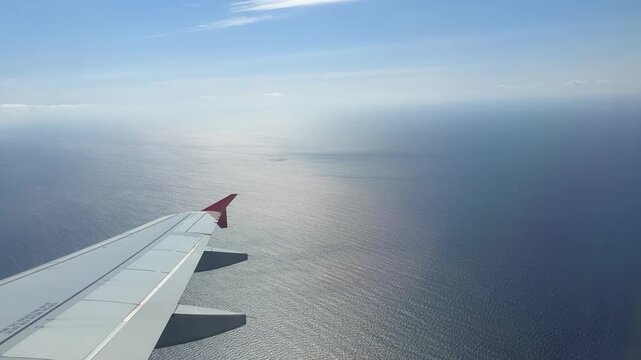 View from the airplane flying over blue calm endless sea surface.Seascape close up with Boeing aircraft wing without logos
