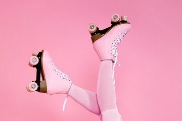 Pink retro roller skates on female legs over pastel pink background