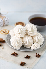 White meringue cookies arranged on a decorative plate, accompanied by a cup of tea and festive decorations, creating a cozy and inviting dessert scene