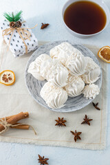 White meringue cookies arranged on a decorative plate, accompanied by a cup of tea and festive decorations, creating a cozy and inviting dessert scene