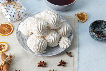White meringue cookies arranged on a decorative plate, accompanied by a cup of tea and festive decorations, creating a cozy and inviting dessert scene