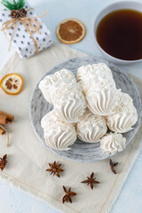 White meringue cookies arranged on a decorative plate, accompanied by a cup of tea and festive decorations, creating a cozy and inviting dessert scene