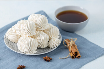 White meringue cookies arranged on a decorative plate beside a cup of dark beverage, with cinnamon sticks and star anise, creating a cozy culinary atmosphere