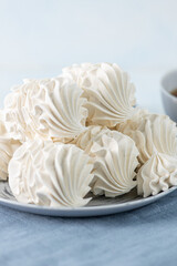 White meringue cookies arranged on a decorative plate beside a cup of dark beverage, with cinnamon sticks and star anise, creating a cozy culinary atmosphere