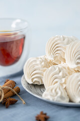 Delicate meringue cookies arranged on a plate, accompanied by a glass of tea, with decorative spices and tea tins in the background, creating a cozy dessert scene
