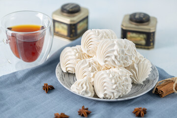 Delicate meringue cookies arranged on a plate, accompanied by a glass of tea, with decorative...