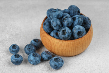 Fresh ripe blueberries in small wooden bowl on gray textured stone background. Delicious organic fruit rich in vitamins, wild berries,healthy lifestyle, natural food. Close up, macro