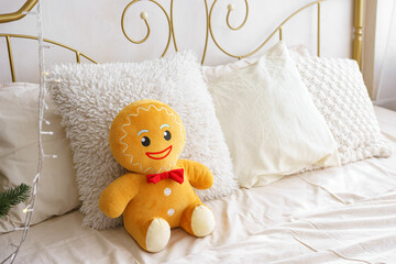 Christmas gingerbread plush toy seated on bed surrounded by fluffy pillows in bright, inviting...