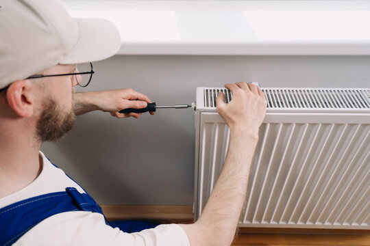 Man performs maintenance on home heating radiator for optimal warmth during winter