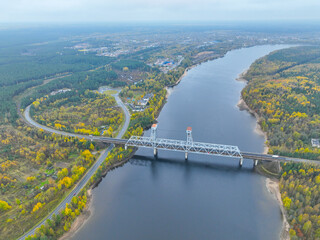 High angle aerial view of a white truss bridge spanning a wide river, surrounded by vibrant autumn forest and roads