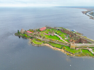 Wide aerial panoramic view of the Oreshek Fortress island in the center, with the water and the distant town in the background