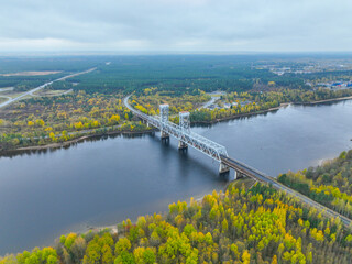 High angle aerial view of a white truss bridge spanning a wide river, surrounded by vibrant autumn forest and roads
