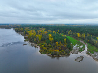 High angle aerial view of a wide river making a bend, surrounded by dense forest with mixed green and yellow autumn foliage