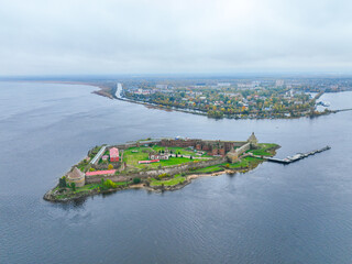 Wide aerial panoramic view of the Oreshek Fortress island in the center, with the water and the distant town in the background