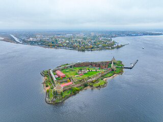 Wide aerial panoramic view of the Oreshek Fortress island in the center, with the water and the distant town in the background