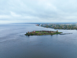 Distant aerial view of the Oreshek Fortress island centered in the wide expanse of the river or lake under a cloudy sky