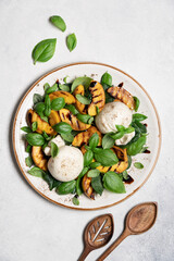 Mediterranean salad with burrata cheese, grilled peaches, fresh basil leaves, olive oil and balsamic glaze, gourmet summer dish on light background