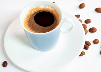 Coffee in a blue cup sits on a white table with coffee beans scattered nearby.