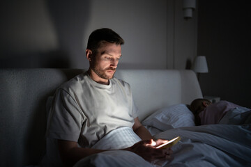 Tired sleepless man procrastinating at night using phone suffer from insomnia. Sleep disorder,...