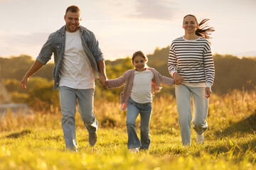 Happy family holding hands and running in field at sunset