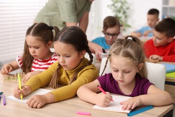 Fototapeta premium Children having lesson with teacher at wooden desk in elementary school, closeup