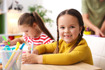 Fototapeta premium Smiling little girls at wooden desk during lesson in elementary school