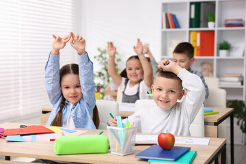 Cute children raising hands at wooden desks during art lesson in elementary school