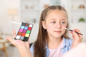 Woman with palette painting girl's face indoors