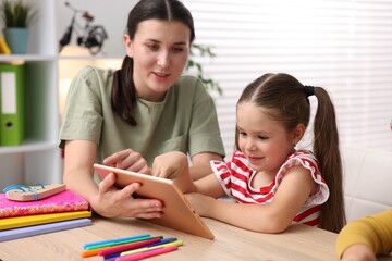Teacher and little girl with tablet at wooden desk in elementary school