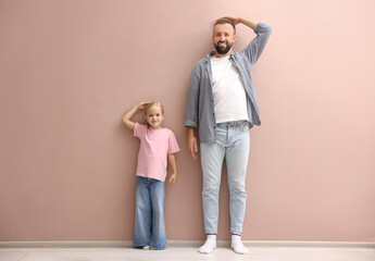 Father and daughter measuring their heights near beige wall indoors