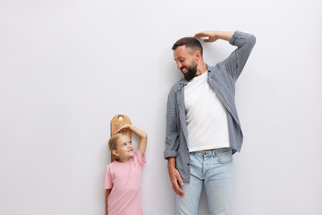 Father and daughter measuring their heights near light wall indoors