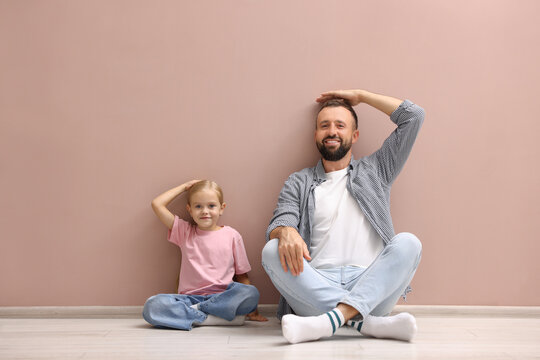 Father and daughter measuring their heights near beige wall indoors - Powered by Adobe