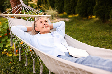 Senior woman with book resting in hammock outdoors