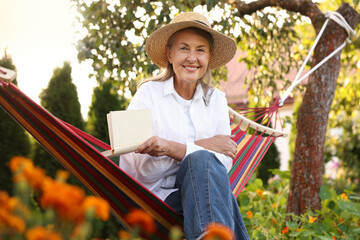 Senior woman with straw hat and book resting in hammock outdoors