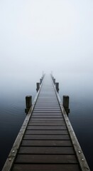 Obraz premium Long wooden pier extending over a placid, fog-laden lake, its dark timbers reflecting subtly on the calm water as it vanishes into the atmospheric mist