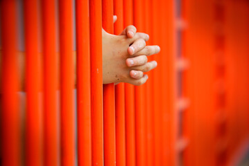 Hands Gripping Bright Orange Bars in Reflective Moment of Contemplation