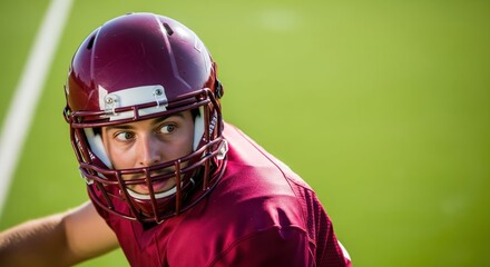 A focused American football player in a maroon helmet and jersey looks over his shoulder with a determined and serious expression on a green turf field under bright sunlight.