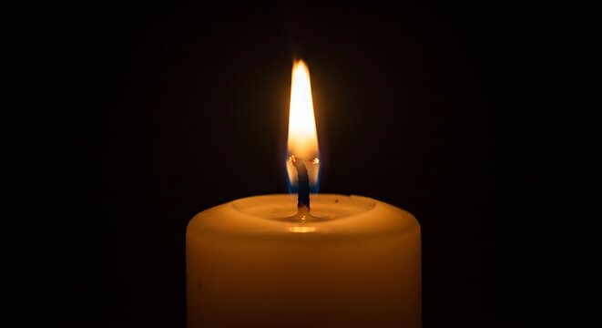 Close up of a lit candle with warm glowing flame against black background