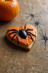 Festive heart-shaped Halloween cookie decorated with orange frosting and a black spider on a rustic table