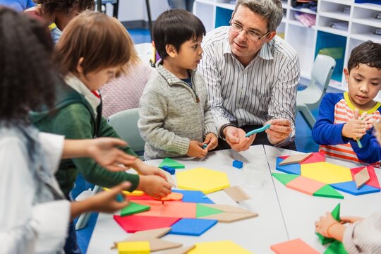 A diverse group of children, including boys and girls in a classroom with teacher. The children and teacher with geometric math shapes in a classroom setting. Diverse kids at elementary school.